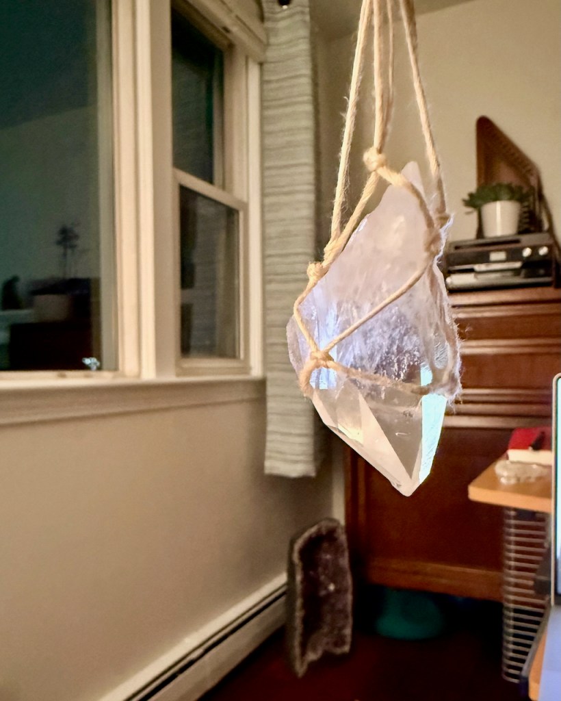 a clear quartz crystal point hanging from a macrame net made of light-colored twine