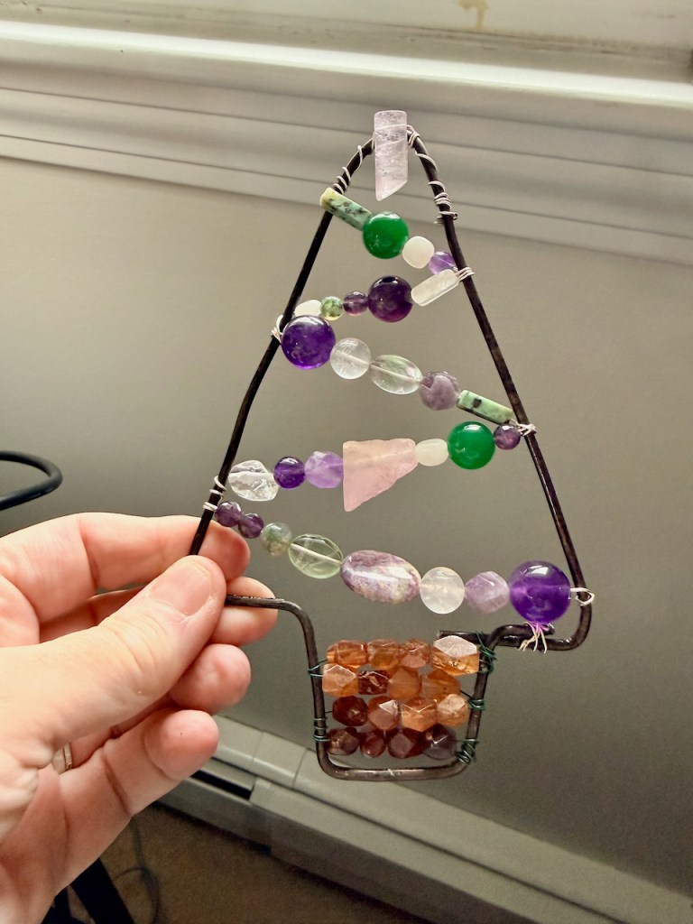 a christmas tree framed from a wire hanger with brown beads for the trunk and purple, white and green beads at angles