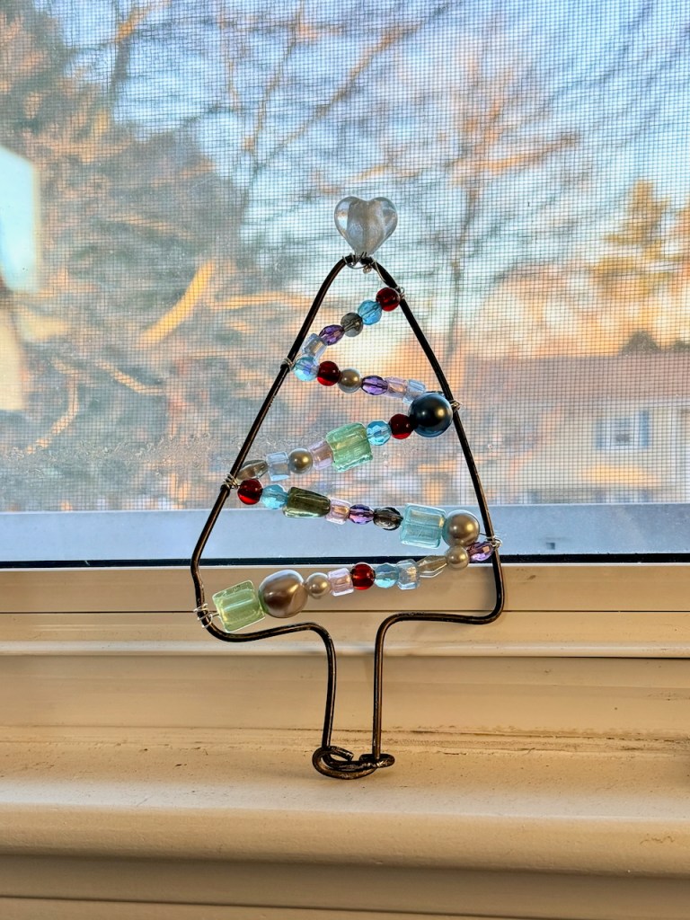 a christmas tree framed from a wire hanger with plastic and glass different colored beads at an angle and a heart=shaped bead as the tree topper