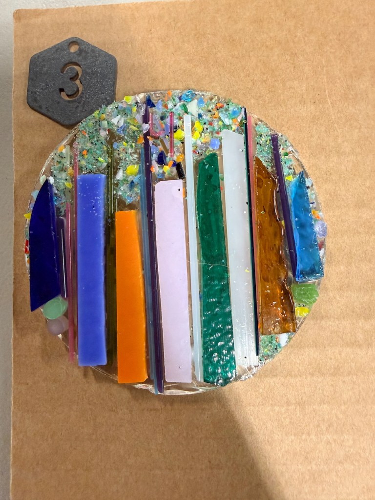 a round ornament with lines of colored glass like candles before it was fired in the kiln