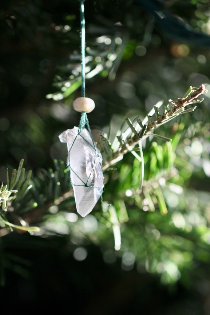 an ornament hanging on a christmas tree. the ornament is a natural clear quartz point with green thread holding it